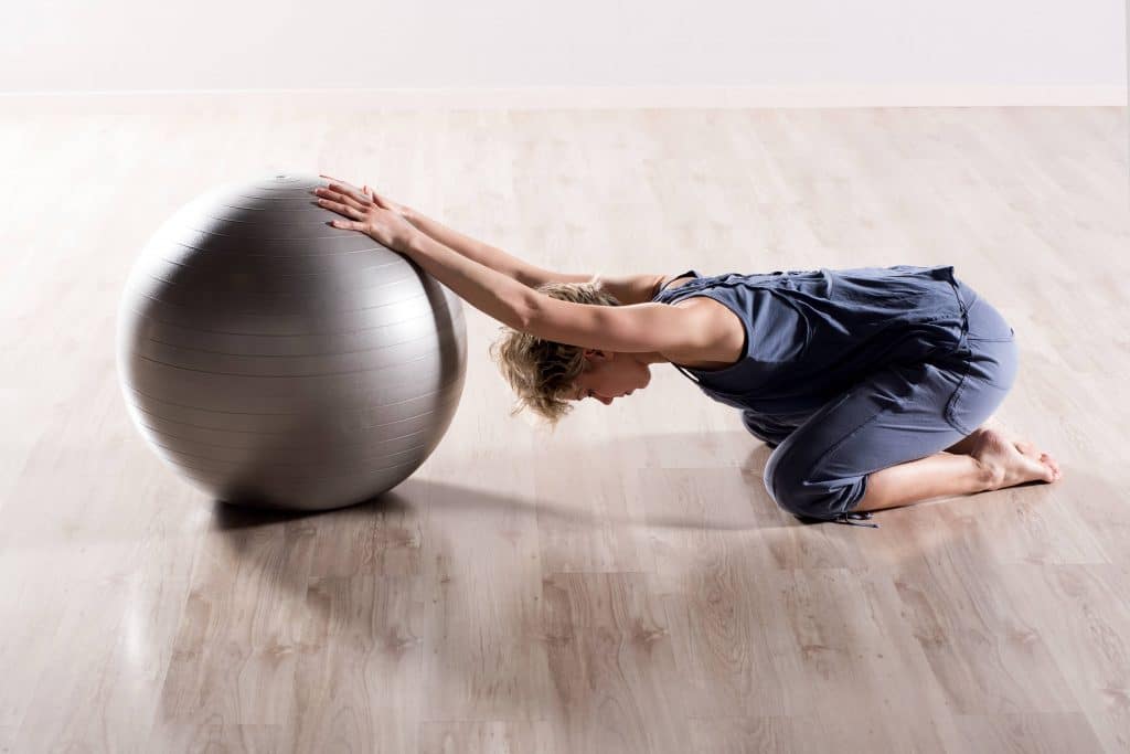 woman stretching her shoulder with an exercise ball