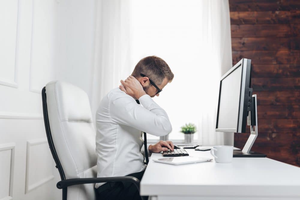 man in his office holding his neck due too neck pain