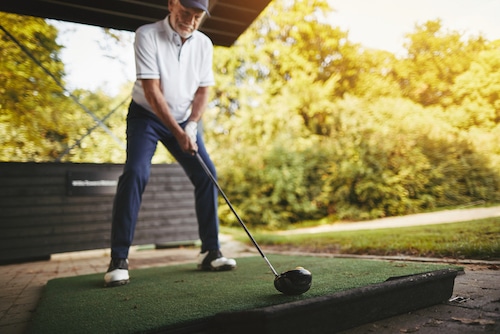 Sporty senior man practicing his swing with a driver at a golf driving range