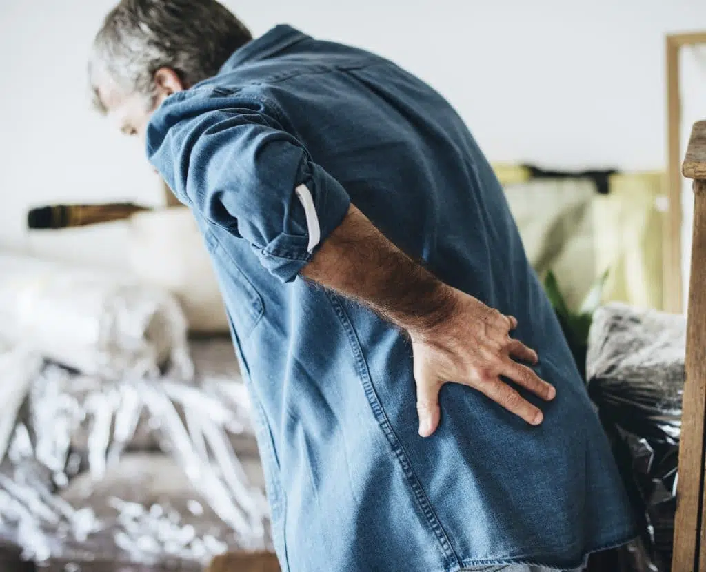 Elderly man holding his lower back due to pain.