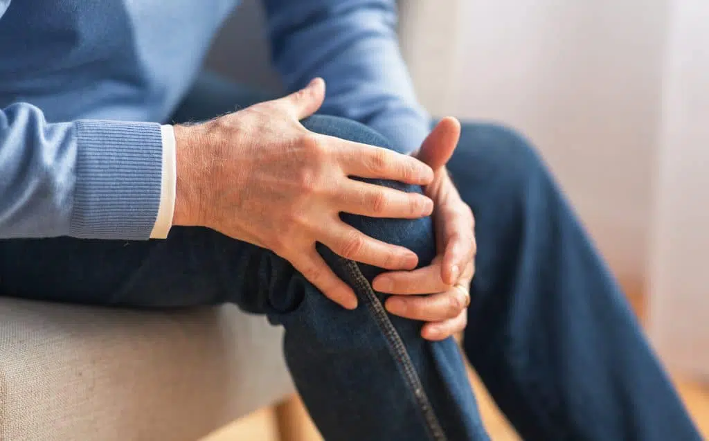 Elderly man holding his knee due to joint pain.