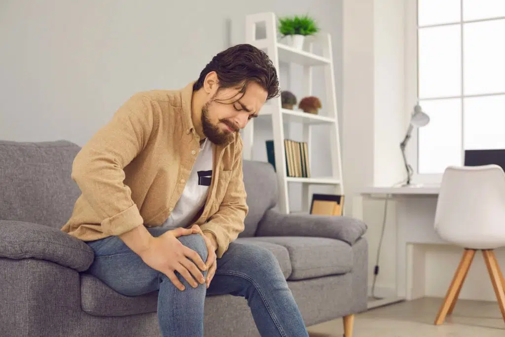 Man sitting on a sofa massaging his knee for knee pain.